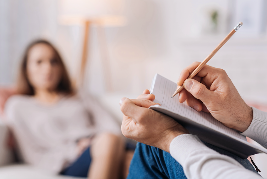 Life-changing benefits of talking therapy - therapist writing in notebook with woman in the background